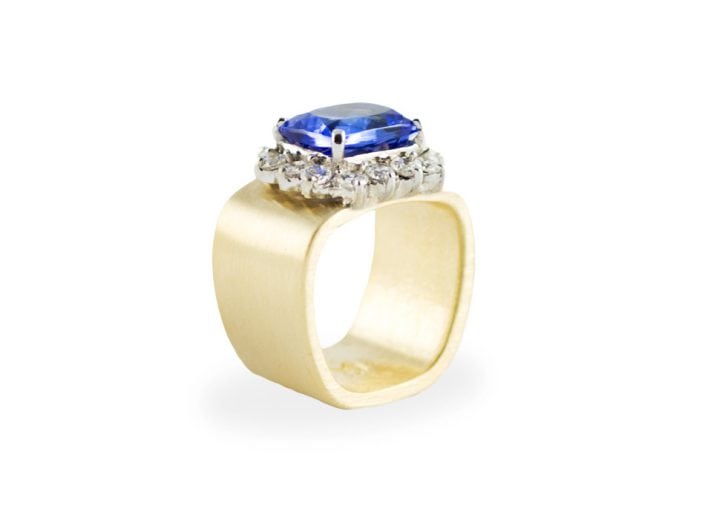 Sparkling 5ct violet blue, cushion-cut tanzanite in a 14k white gold setting atop a brushed 14k yellow gold square band. The bezel includes 14 round diamonds for a total of 1.2 ctw.