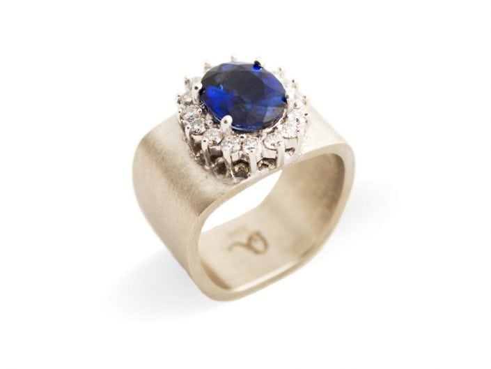 Stunning blue sapphire surrounded by 16 white diamonds atop a square 14k white gold band.