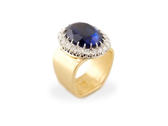 Stunning, large oval sapphire surrounded by diamonds in a 14k white gold setting atop a brushed 14k gold band.